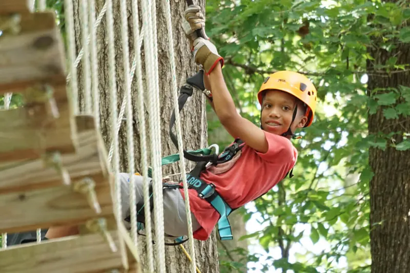 Summer camper climbing a rope ladder in a helmet and harness